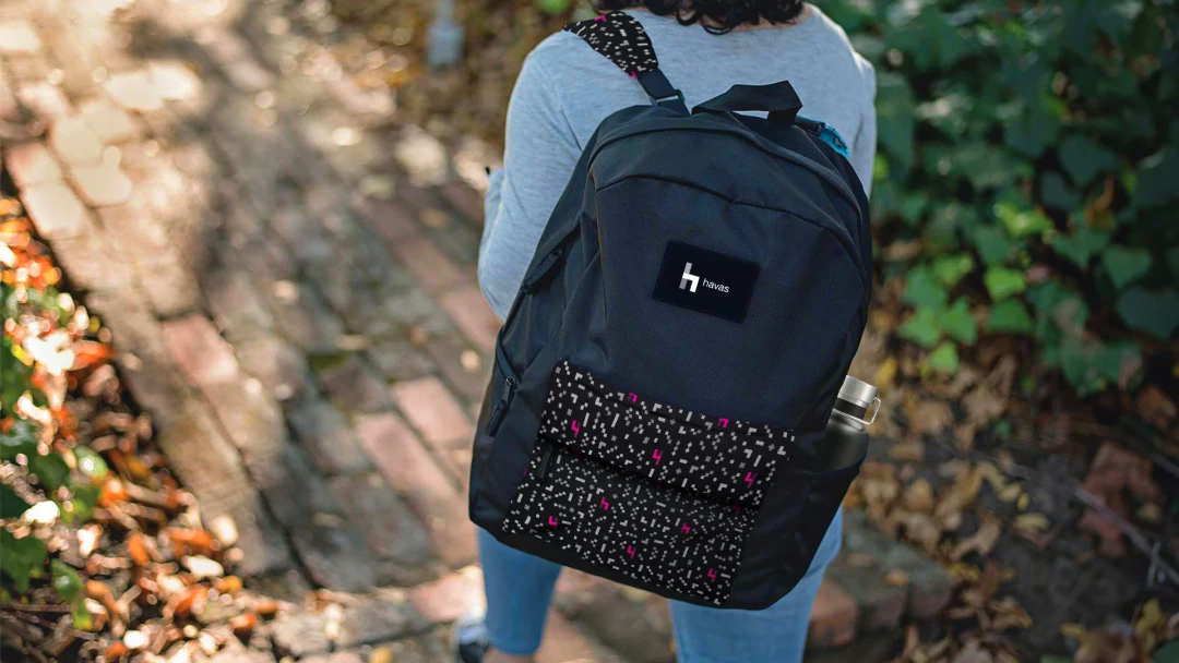 A person wearing a fully customized digitally printed backpack featuring a creative design and the Havas Media logo, showcasing the power of custom branded merch and promotional products for B2B business services from Brand Blvd.