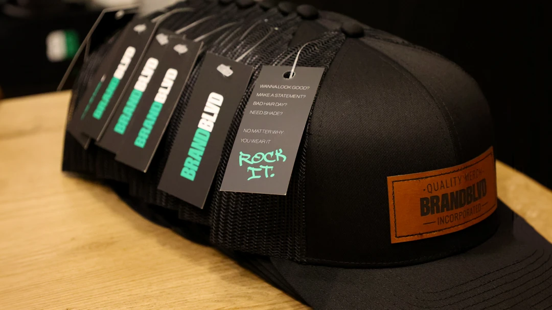Black hats with a leather patch sitting on a table, with custom hang tags attached.