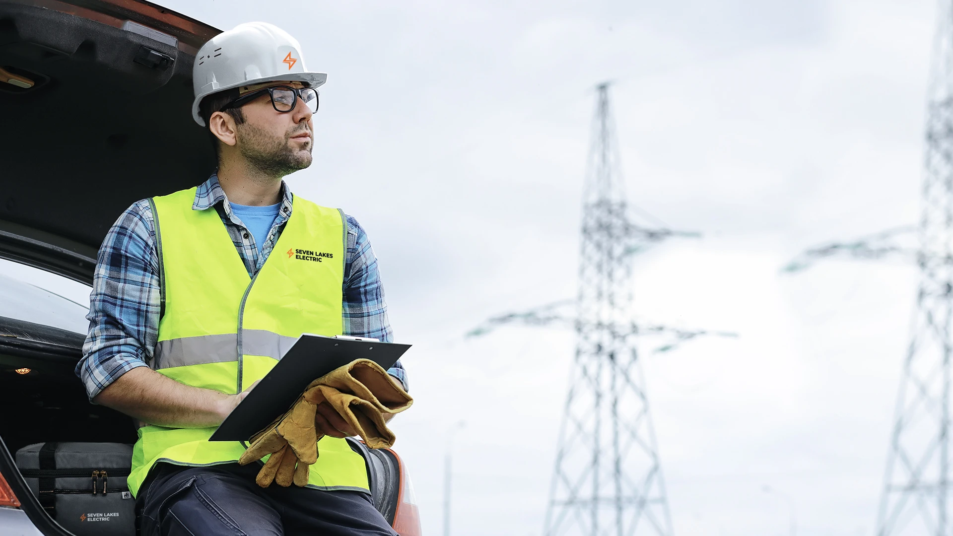 An energy utility worker wearing a branded safety vest and hard hat, at an electricity work site with a Heritage Supply Pro XL Lunch Cooler.