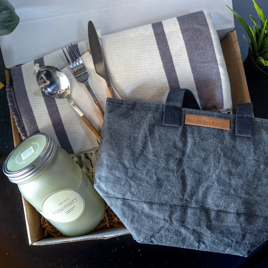 An eco sustainable branded merch kit which includes an Out of the Woods stone paper cooler bag, reusable utensil set, organic cotton blanket and a grow-your-own herb kit. An example of environmentally-friendly logo merch from Brand Blvd