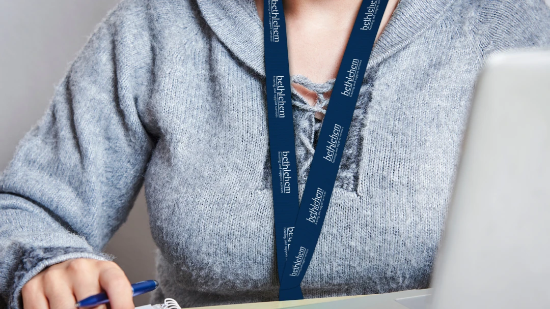 Person wearing a lanyard branded with the Bethlehem Housing and Support Services logo. Showcasing support for a meaningful non-profit, donor engagement, and raising awareness with promotional products and merch from Brand Blvd.