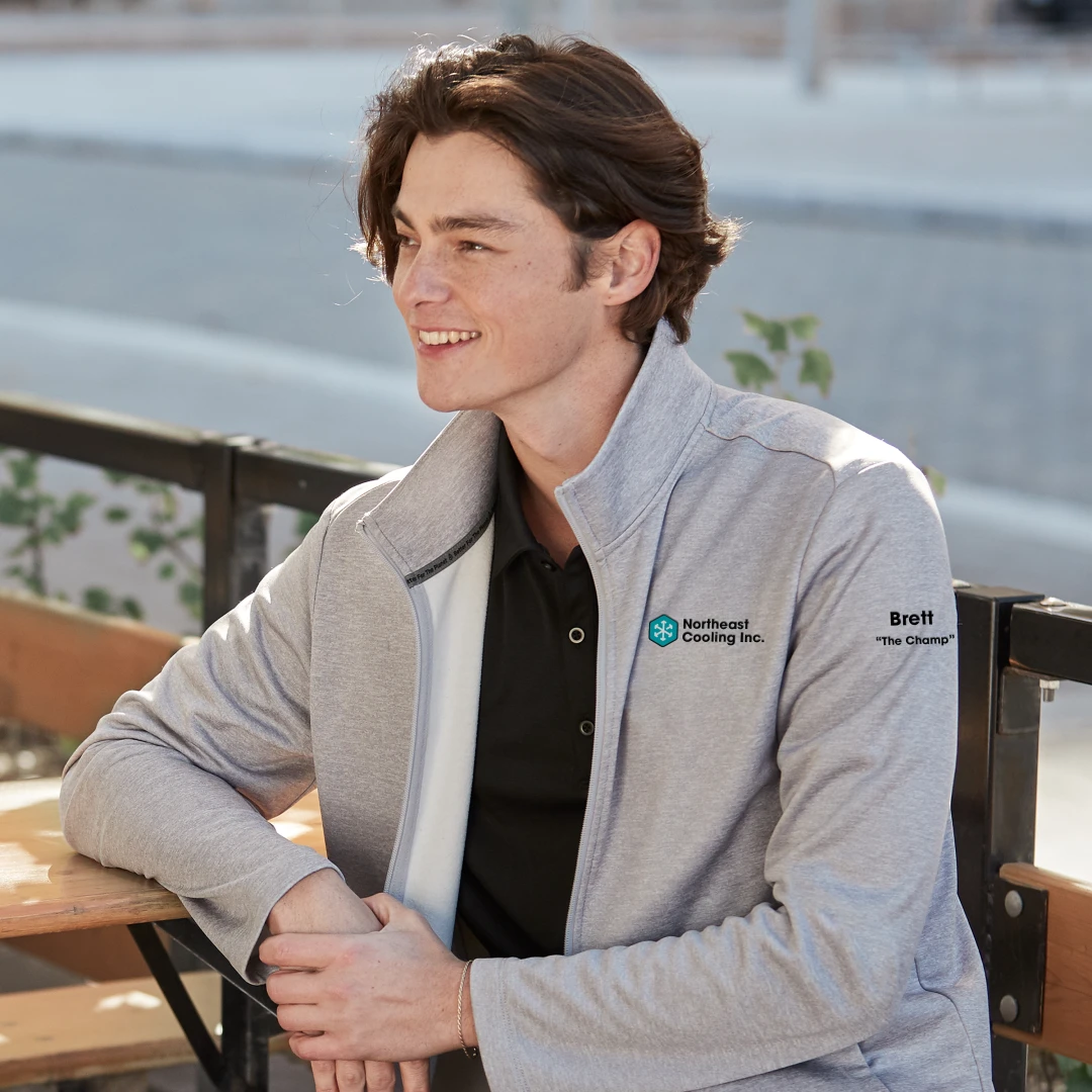 An employee wearing a sweater branded with their company logo and personalized with their nickname. An example of merch from Brand Blvd that cultivates belonging and positive workplace culture.