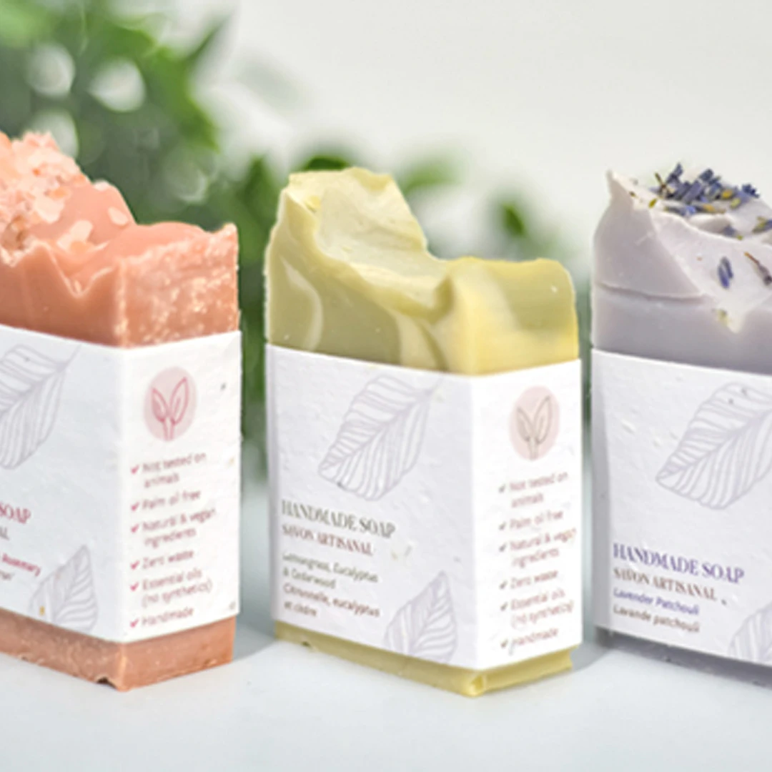 A photo of 3 hand-crafted artisanal soaps. Coloured pink, green and purple, with branded botanical seed paper belly bands.