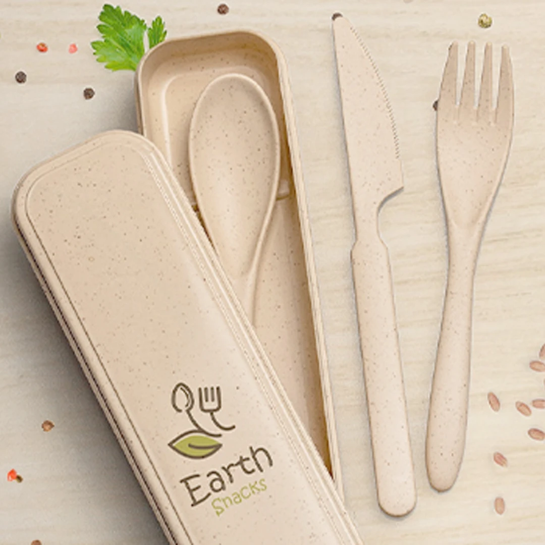 A photo of a set of reusable wheat straw material cutlery in a branded container on a wood table. 