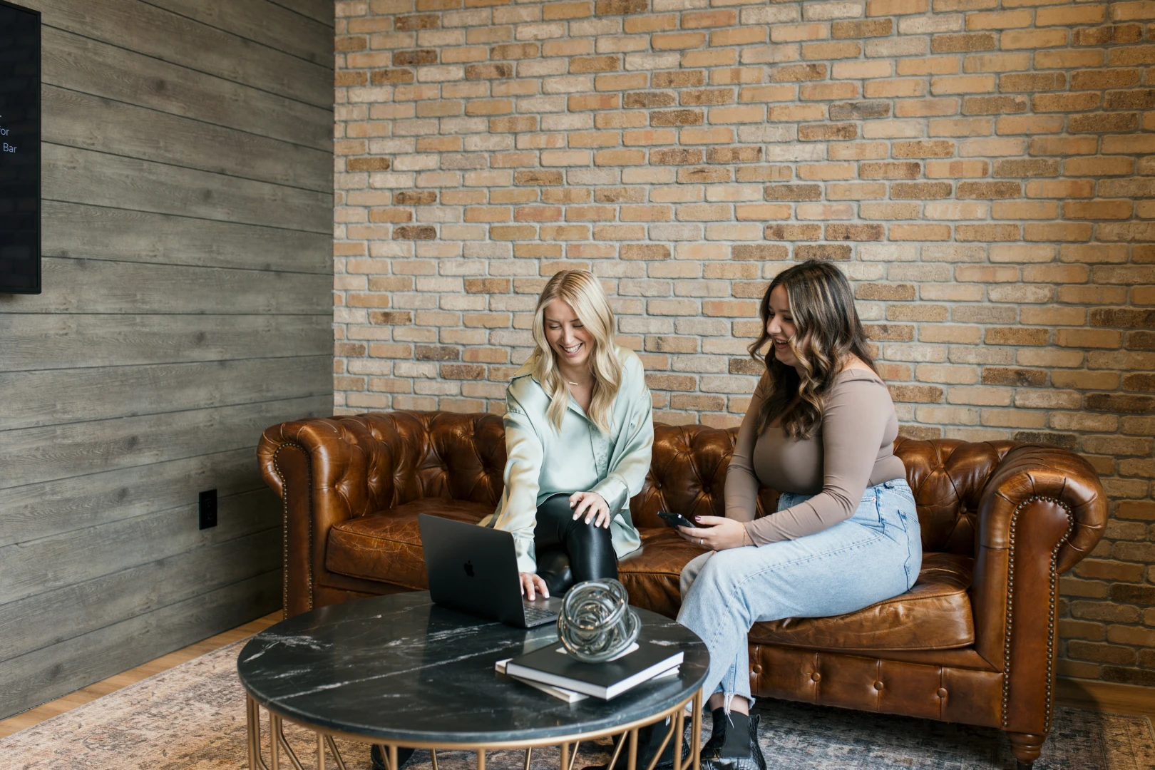 A photo of a 2 people on a laptop collaborating while sitting on a brown leather couch