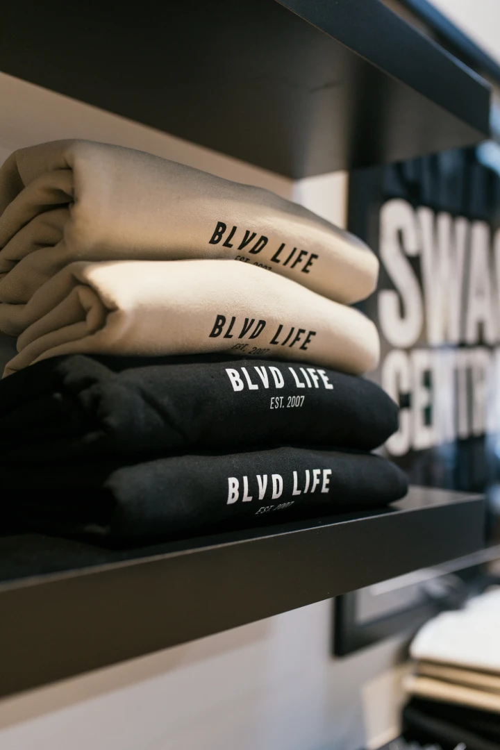 A photo of BB Life crewnecks in black and cream stacked on a shelf.