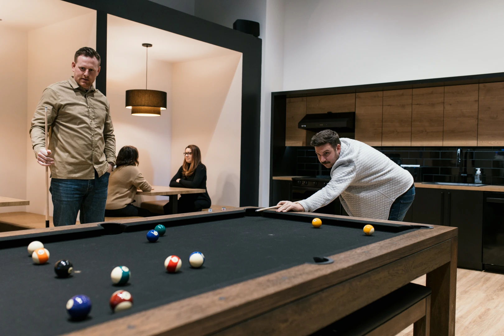 A photo of the Brand Blvd lunch room with 2 people playing pool and 2 other talking at a booth.