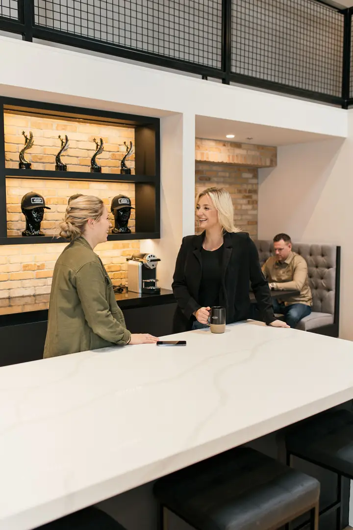 A photo of 2 women conversing and a man on a laptop in the Brand Blvd great room.