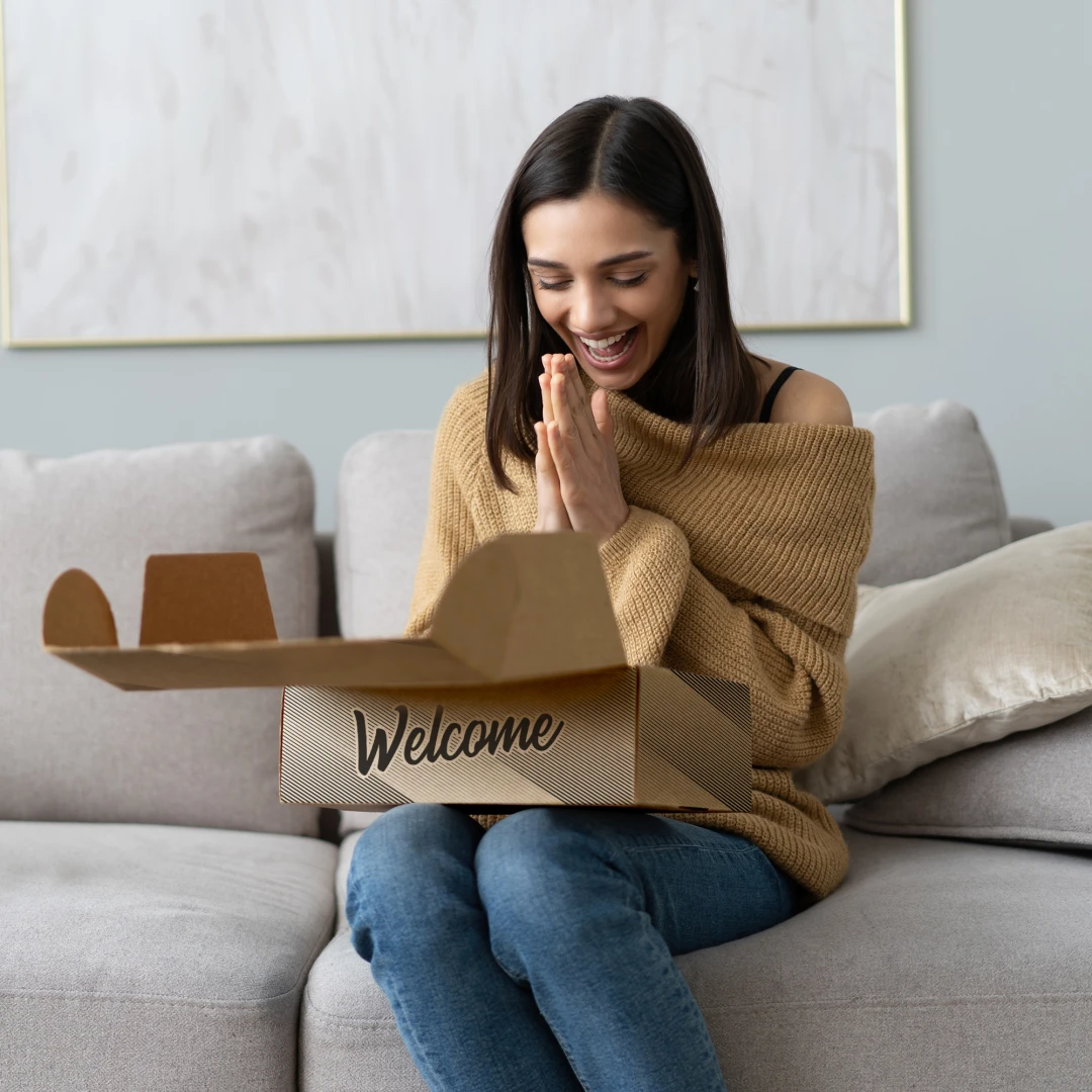 A photo of a woman on her couch looking very excited while opening a custom printed swag kit.