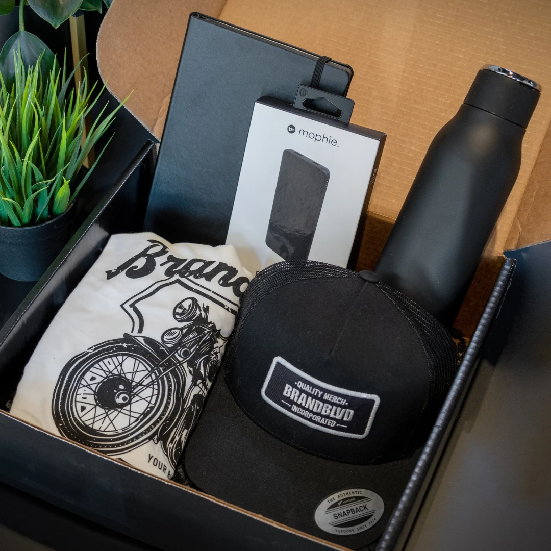 A photo of the Yay First Day curated swag kit which includes a black water bottle, notebook, wireless charger, T-shirt and a hat.