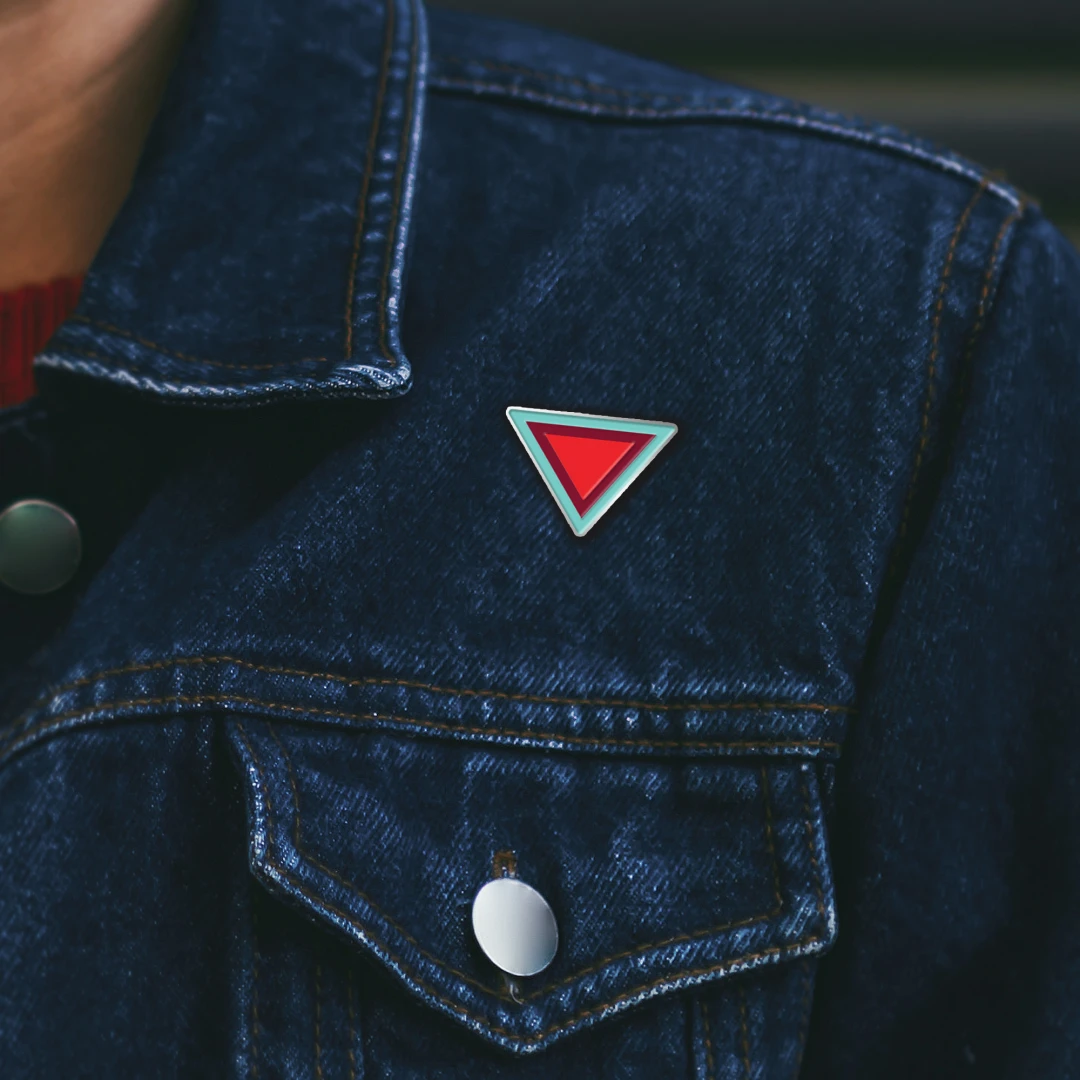 A close up photo of a dark denim jacket pocket with enamel pins.