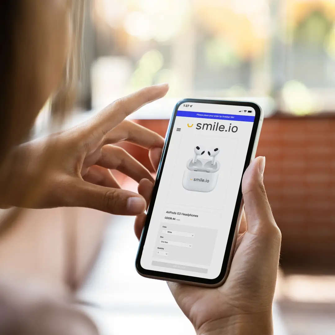 A photo of a person holding up an iPhone with the Smile.io online store wireless earbuds product page on screen.