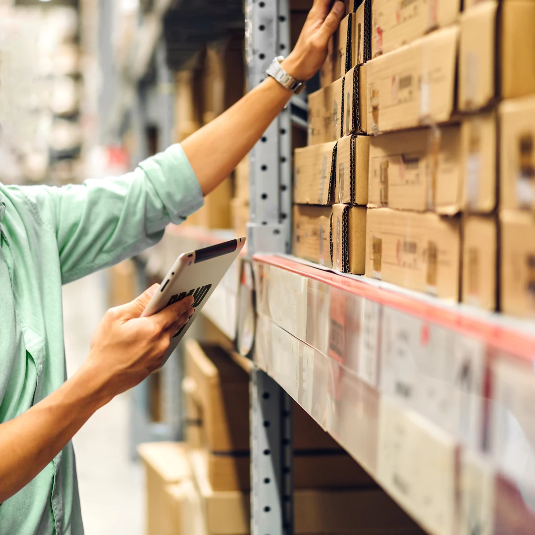 A photo of a person at a shelf in a warehouse with an ipad in their had.